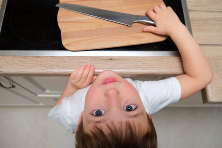 Little boy child playing with knife on kitchen stove. Danger and risk for kid alone at home. Supervise children concept. Child aged 4 years (four years old)の写真素材