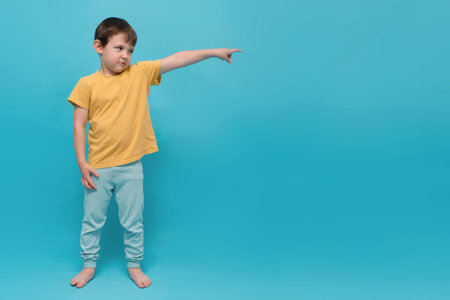 Little boy child in yellow t-shirt pointing finger to side, looking curious and surprised. Young kid with a expressive face shows direction to empty space.の写真素材
