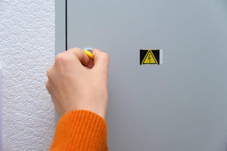 A woman's hand using a yellow key to open an electrical panel. Safety and maintenance concept for...
