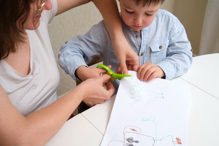 Woman helping a little boy with cutting out a drawing from paper. Early childhood education and development, fine motor skills training for kids. A child aged 4 years (four years old)の写真素材