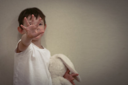 Small child raises hand in a stop gesture while holding a stuffed toy, symbolizing domestic violence, fear, and need for protection. Copy spaceの写真素材