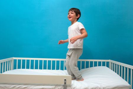Little boy jumping on a bed with a blue background, expressing joy and energy. Playtime and happy childhood concept. Child aged 4 years (four years old)の写真素材