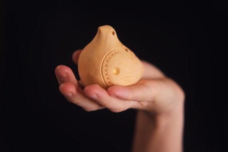 Woman holding a small ceramic bird-shaped ocarina in her palm. Traditional clay flute instrument on a black background for music.の写真素材