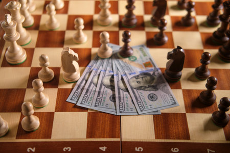 A chessboard with white and black chess pieces and several one hundred dollar bills. Game strategy and financial investment concept.の写真素材