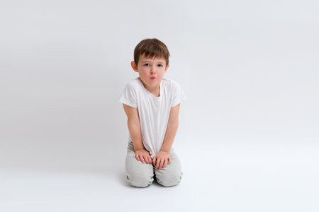 Caucasian kid making a fish face while kneeling on a white background. Funny childhood emotion concept for children's content. Child aged 4 years (four years old)の写真素材