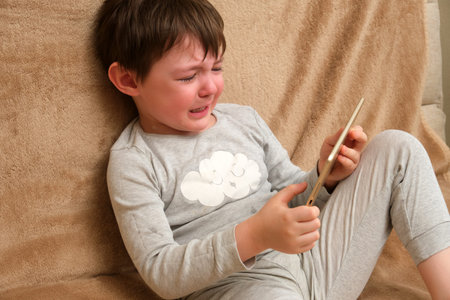 Crying boy holding a digital tablet. Child problem with screen time and technology addiction....