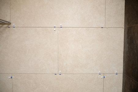 Beige ceramic wall tile recently installed with leveling spacers. Home renovation process in bathroom or kitchen. Professional construction work, interior finish and material texture.の写真素材