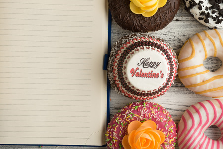 Donut with icing on a white wooden background. Next to lies a notebook to record the recipes of donuts. The Concept Of Valentine's Dayの写真素材