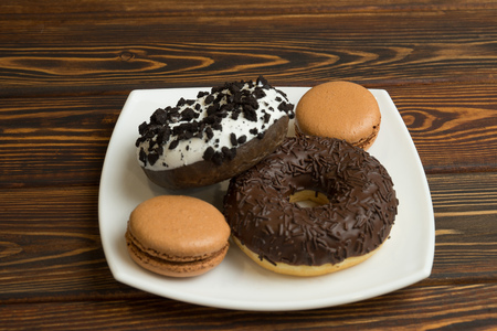 Chocolate donuts with icing and macaron lie on a plateの写真素材