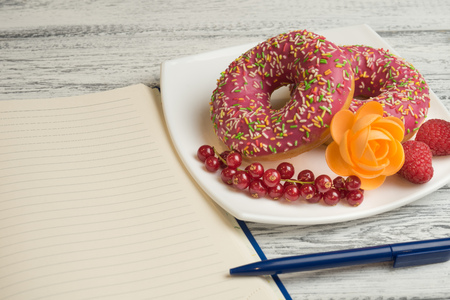 Donuts with icing and berries on the plate Next to lies a notebook to record the recipes of donutsの写真素材