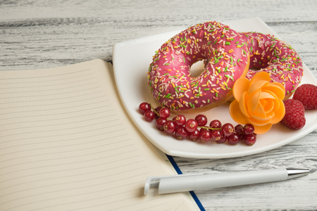 Donuts with icing and berries on the plate Next to lies a notebook to record the recipes of donutsの写真素材