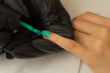 A manicurist makes manicure and covers nails with green varnish in the salonの写真素材