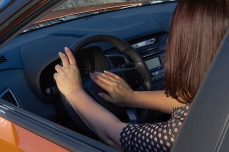Close-up inside car of hand pushing on steering wheel honking horn, female driver concept