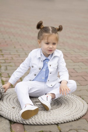 Stylish little baby is sitting on the ferry cable on the marina. She is dressed in fashionable designer clothesの写真素材