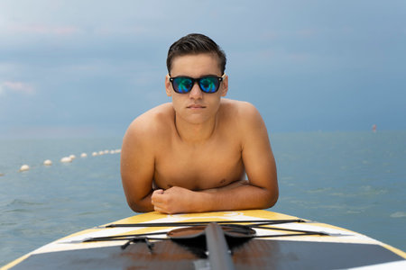 Fashion model in sunglasses posing in the water with sup surfboard. Water sports, fashion and styleの写真素材