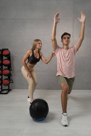 Young man working out with personal trainer at the gym. Exercises with ballの写真素材