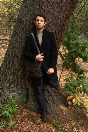 Portrait of a young, stylish man with leather handbag in the parkの写真素材