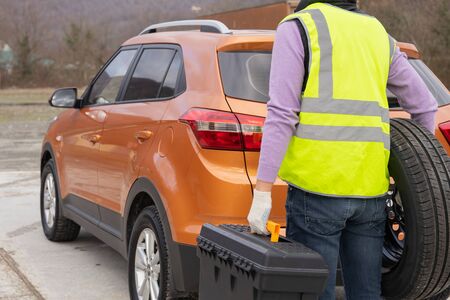 Emergency roadside assistance, technician wearing a high-visibility vest helps with wheel replacement.の写真素材