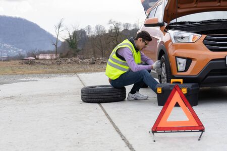 A mechanic in a reflective vest changes a wheel on the roadの写真素材