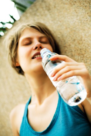 young blond woman with closed eyes drinking water from plastic bottle standing near the wall blurred faceの写真素材