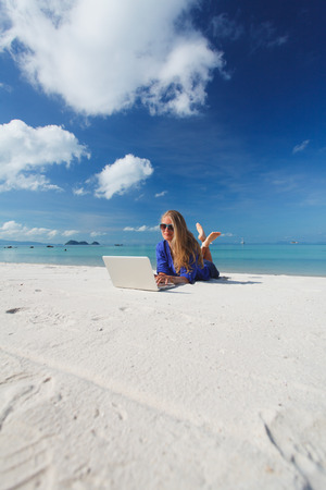 Beautiful young woman working with laptop on the tropical beachの写真素材