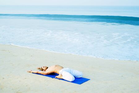 Long Hair Athletic Man with No Shirt doing Yoga on Blue Mat at the Beachの写真素材