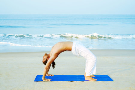 Long Hair Athletic Man with No Shirt doing Yoga on Blue Mat at the Beach