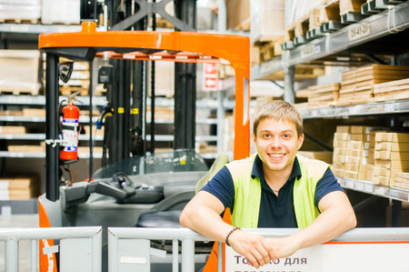 young man in working clothes, driver Reachtruck busy working on the logistics warehouse storeの写真素材