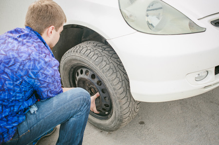 man changing a wheel on the road. on way there was breakage of wheel, puncture, necessary to lift the car jack and remove the wheel by loosening the nuts. road problems travelers. do it yourselfの写真素材