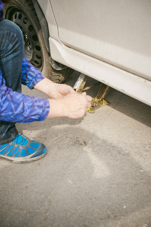 man changing a wheel on the road. on way there was breakage of wheel, puncture, necessary to lift the car jack and remove the wheel by loosening the nuts. road problems travelers. do it yourselfの写真素材