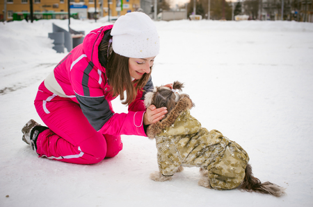 Walk in winter outdoors with dog breed Shih Tzu. A woman in bright red warm ski clothing walking in snow with your pet, little shih tzu dressed in overalls. care for animals loves playing with the dogの写真素材