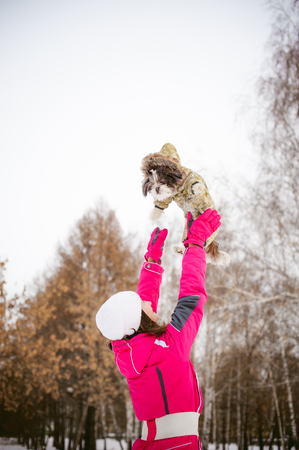 dog throws up into the sky. Walk in the winter outdoors with a dog breed Shih Tzu. A woman in a bright red warm ski clothing walking in the snow with your pet, a little shih tzu dressed in overalls. care for animals, and loves playing with the dogの写真素材