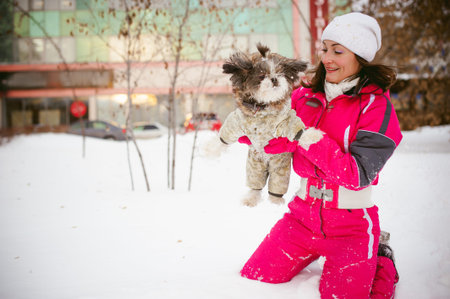 Walk in winter outdoors with dog breed Shih Tzu. A woman in bright red warm ski clothing walking in snow with your pet, little shih tzu dressed in overalls. care for animals loves playing with the dogの写真素材