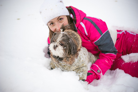 Walk in winter outdoors with dog breed Shih Tzu. A woman in bright red warm ski clothing walking in snow with your pet, little shih tzu dressed in overalls. care for animals loves playing with the dogの写真素材