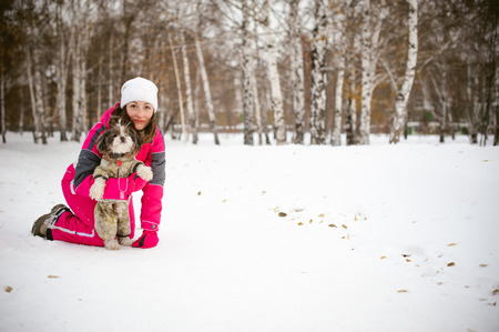 Walk in winter outdoors with dog breed Shih Tzu. A woman in bright red warm ski clothing walking in snow with your pet, little shih tzu dressed in overalls. care for animals loves playing with the dogの写真素材