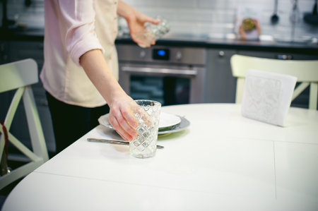 blonde woman housewife doing the work in the kitchen, setting the table, puts the dishes and cutlery. home in the kitchen in a bright interiorの写真素材