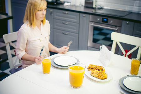Pretty blonde woman in a pink shirt, eating at home. breakfast sandwich and peach juice. on white...