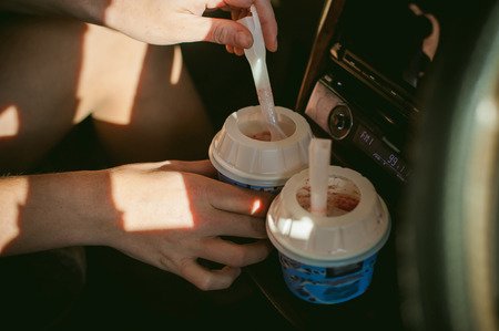 girl eating ice cream with a spoon in the car. blond girl in a raincoat, eats ice cream while in the car during a road tripの写真素材