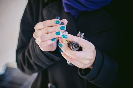 portrait of young beautiful woman with white hair, in a black coat, a skirt and a black hat, smoking an electronic cigarette, runs vape juice electronic cigarette. He holds a mechanical mod with RDA.の写真素材