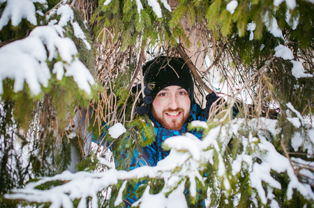 men walk in a winter park. guy with good humor and smile, warm clothing walking outdoors, looking out of coniferous treesの写真素材