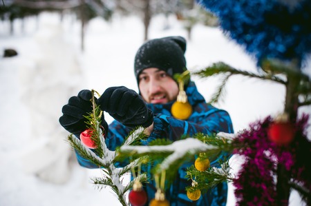 men walk in a winter park. guy with good humor and smile, warm clothing walking outdoors, dress up a Christmas tree decorations on the streetの写真素材