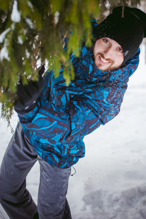 men walk in a winter park. guy with good humor and smile, warm clothing walking outdoors, looking out of coniferous treesの写真素材