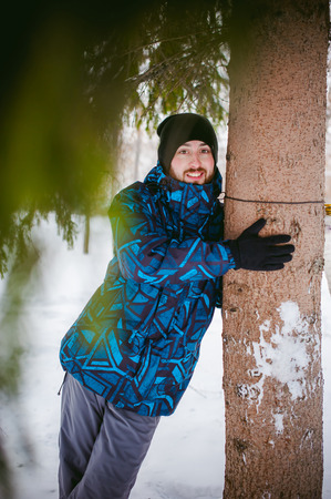 men walk in a winter park. guy with good humor and smile, warm clothing walking outdoors, looking out of coniferous treesの写真素材