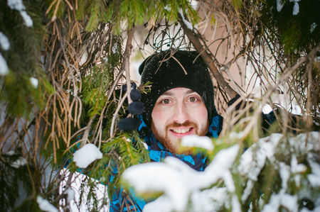 men walk in a winter park. guy with good humor and smile, warm clothing walking outdoors, looking out of coniferous treesの写真素材