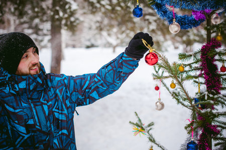 men walk in a winter park. guy with good humor and smile, warm clothing walking outdoors, dress up a Christmas tree decorations on the streetの写真素材