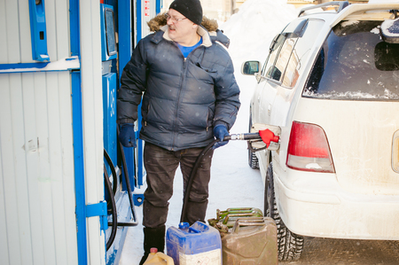 adult man fills a car with petrol at a fuel station in the winter. refueling nozzle man holding in his hand, pouring the liquid in the canister and fuel tankの写真素材