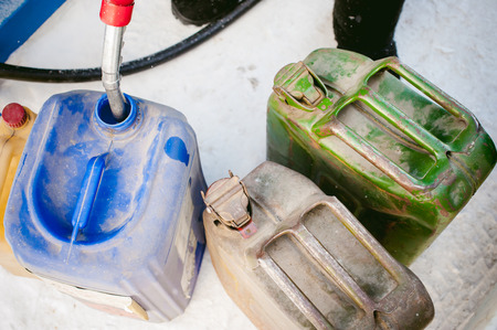 adult man fills a car with petrol at a fuel station in the winter. refueling nozzle man holding in his hand, pouring the liquid in the canister and fuel tankの写真素材