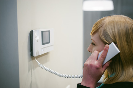 blonde woman answers the intercom call while holding the phone to your earの写真素材