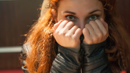 portrait of a woman with her hands covering the face, with bent fingers, thick red hair with braids sitting in cafeの写真素材
