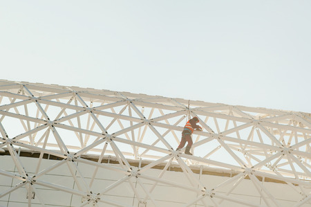 man in overalls  builder fixes on the height. Assembling, refurbishment works at altitude with metal structure, outdoors against the skyの写真素材